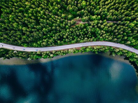 Aerial view of road between green summer forest and blue lake in Finlandの写真素材
