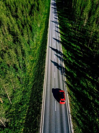 Aerial view of a country road with red car in the middle of green summer forest in rural Finlandの写真素材