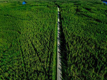View of a country road with red car in the middle of green summer forest in rural Finlandの写真素材