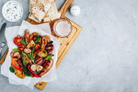 Grilled vegetables and sausages on wooden board, top viewの写真素材