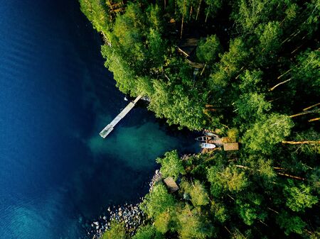 Aerial view of green forest, blue lake and wooden pier with fishing boats in Finland.の写真素材