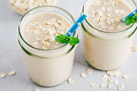 Banana oats smoothie or milkshake in glass mason jars on a gray stone backgroundの写真素材