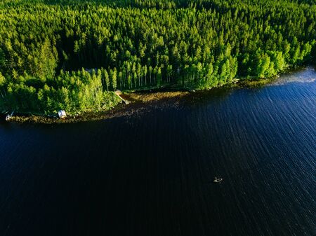 Aerial view of blue lake with a fishing boat and green woods on a sunny summer day in Finland. Drone...