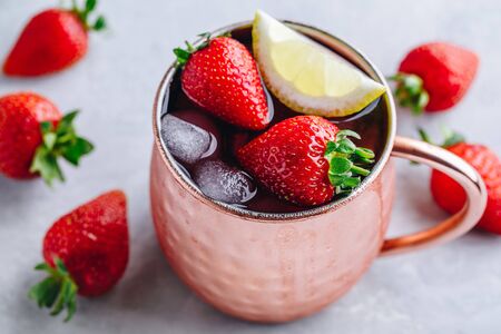 Refreshing iced Moscow mule alcoholic cocktail in copper mugs with strawberry and lemon on gray stone background.の写真素材
