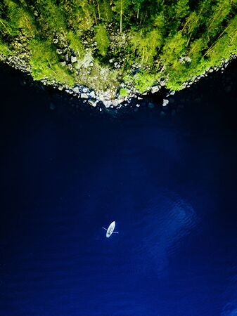 Aerial view of blue lake with a fishing boat and green forests with rocks on a summer day in Finland.の写真素材