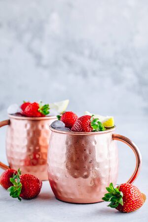 Refreshing iced Moscow mule alcoholic cocktail in copper mugs with strawberry and lemon on gray stone background.の写真素材