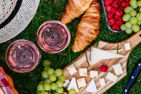 Picnic at the park on the grass. Cheese, raspberry, grape, croissant, baguette, rose wine. Top viewの写真素材