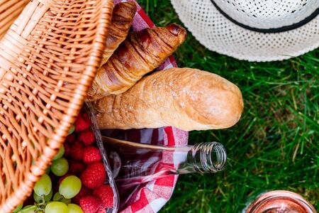 Picnic at the park on the grass. Basket with food, raspberry, grape, croissant, baguette.  Top viewの写真素材