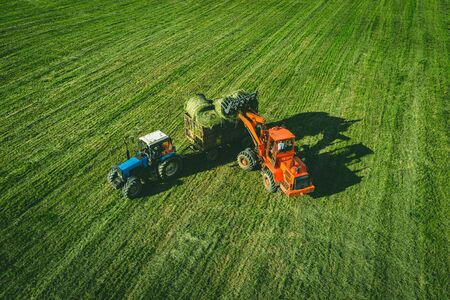 Aerial view of tractor with round baler rolling bales of straw on harvested field. View from aboveの写真素材
