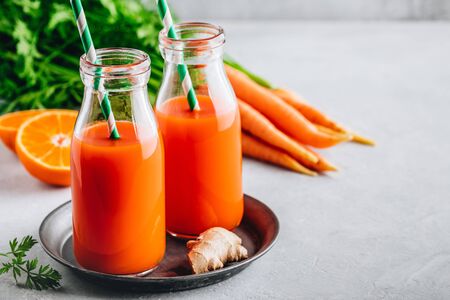 Fresh detox carrot, ginger and orange drink in glass bottles on a gray stone backgroundの写真素材