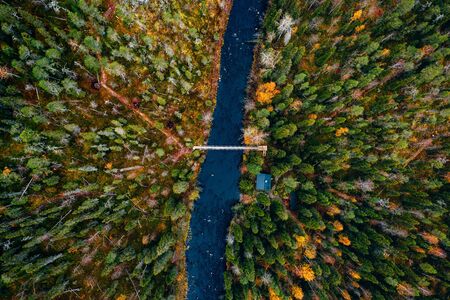Aerial view of river with suspension bridge and log cabin or cottage in colorful autumn forest in Finland Lapland.の写真素材