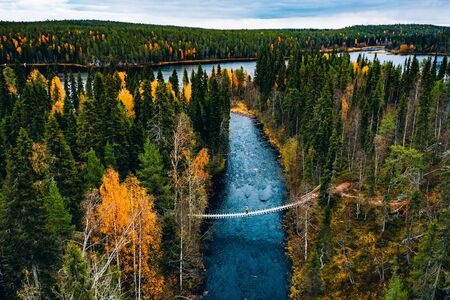 Aerial view of river with suspension bridge in colorful autumn forest in Finland Lapland.の写真素材