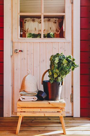 Sauna accessories with birch broom, hat and towels near a traditional red wooden sauna in Finlandの写真素材
