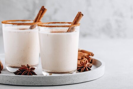 Homemade vanilla Christmas drink Eggnog in glass with grated nutmeg and cinnamon sticks on gray stone background. の写真素材
