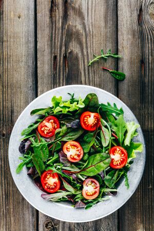Mix of fresh green salad leaves with arugula, lettuce, spinach, beets and tomatoes on wooden rustic background. Top view.の写真素材