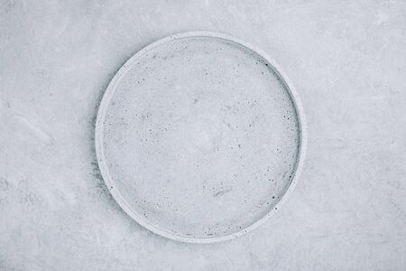 Empty round stone plate on gray concrete background, top view, copy space