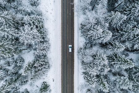 Aerial view of winter road with a car and snow covered trees in the forest in Finland