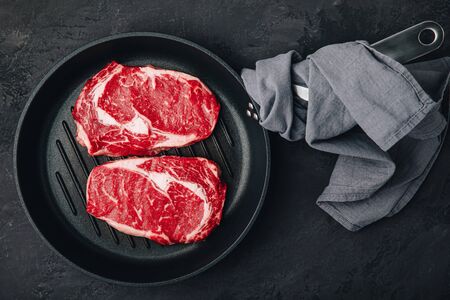 Ribeye Steak, Raw fresh beef meat in grill pan on dark stone backgroundの写真素材