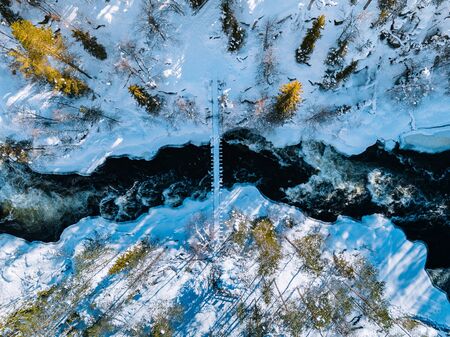 Aerial view of fast river with suspension foot bridge. Snow winter forest in Finland, Oulanka...