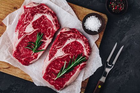Ribeye Steak, Raw fresh beef meat with salt and rosemary ready for barbecue on dark stone backgroundの写真素材