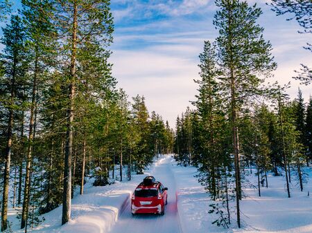 Red car with roof rack driving on snow forest road in winter in Finland.
