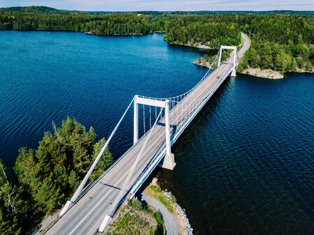 Aerial view of white suspension bridge with car crossing over deep blue lake in rural summer Finlandの写真素材