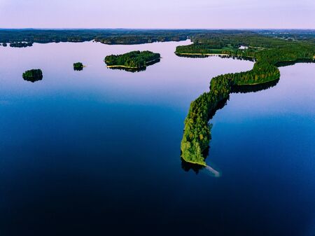 Aerial view of blue lakes with islands and green forests on a summer day in Finland.