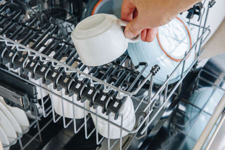 Dishwasher machine close-up. Woman hand taking out clean dish after washing.の写真素材