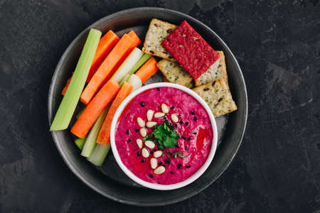 Beetroot Beet Hummus with fresh vegetables and crispbread. Healthy vegan dip on dark stone background, copy space.の写真素材