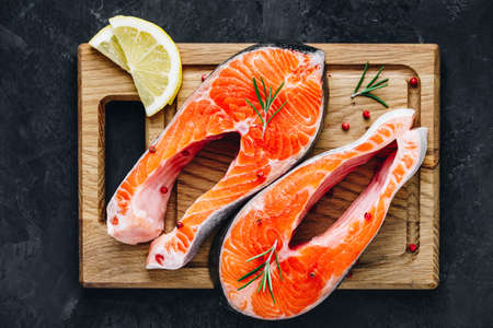Fresh raw Salmon Steaks on wooden board prepared for cooking. Top view, copy space on dark stone background.の写真素材