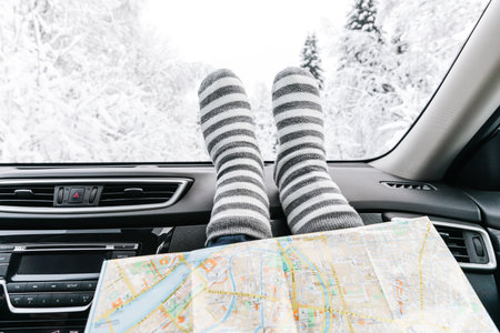 Woman feet in warm socks on car dashboard and travel map. Snow winter time, travel concept.の写真素材