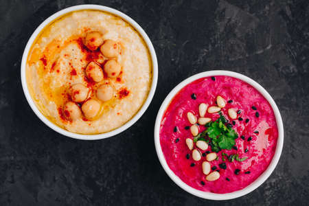 Beet hummus and classic hummus with crisp bread in bowls on dark stone background. Healthy vegan dips, top view.の写真素材