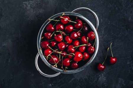 Cherry. Fresh organic sweet cherries in colander on dark stone background. Top view with copy space