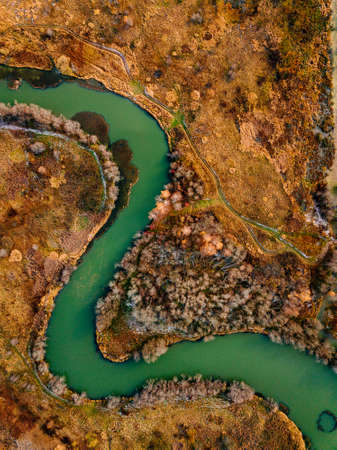 Aerial view of winding river and road in golden colored autumn or fall forestの写真素材