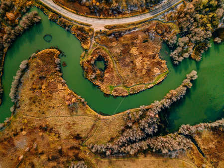 Aerial view of winding river and road in golden colored autumn or fall forestの写真素材
