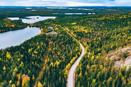 Aerial view of rural road in yellow and orange autumn forest with blue lake in Finland, Lapland.の写真素材