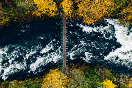 Aerial view of fall forest and blue river with bridge in Finland. Beautiful autumn landscape.の写真素材
