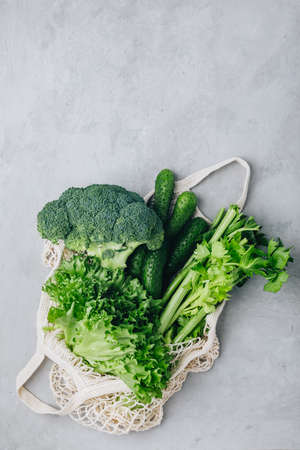 Mesh bag with vegetables. Organic Broccoli, celery, cucumbers, lettuce in cotton shopper bag on gray stone background. Zero waste, plastic free concept. Healthy clean eating diet and detox. Top view with copy space.の写真素材