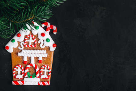 Gingerbread House Cookie. Homemade Gingerbread House Cookie with christmas fir tree branch on dark stone background. Top view with copy space. Christmas bakery. Festive traditional cookies.の写真素材