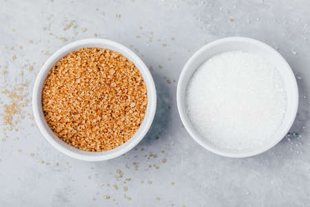 White and Brown sugar in bowls on gray stone background, top view