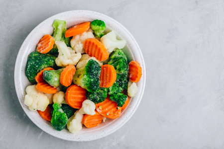 Frozen vegetables. Frozen carrots, broccoli and cauliflower in bowl on gray stone background, top view with copy spaceの写真素材