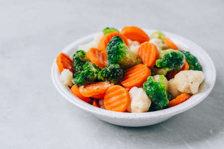 Frozen vegetables. Frozen carrots, broccoli and cauliflower in bowl on gray stone background, copy spaceの写真素材