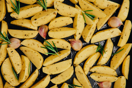 Raw potato wedges with oil, rosemary and garlic on baking tray, preparing to bake. top viewの写真素材