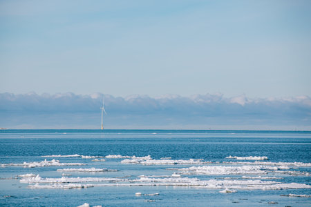 Aerial view Wind turbine by blue sea in snow winter landscape in Finland, Europe. Alternative energy...