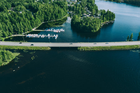 Aerial view of road with cars over blue lake in Finland. Beautiful summer landscape, marina with fishing boats and town in green woodsの写真素材