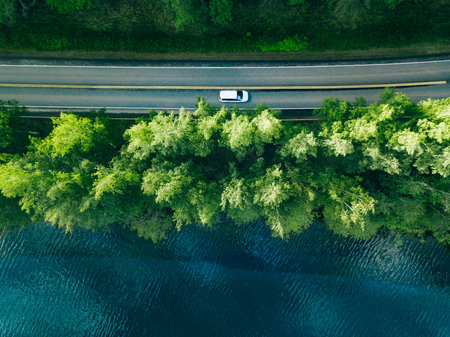 Aerial view of road between green tree forest and blue lake sea water in summer Finland