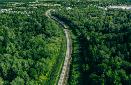 Aerial drone view of train in beautiful green summer forest. Long commuter train moving to railway...