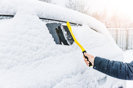 Man cleaning car from snow with yellow brush in winter time. Removing snow from car windows.の写真素材