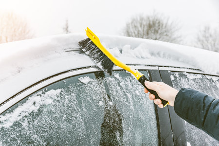 Man cleaning car from snow with yellow brush in winter time. Removing snow from car windows.の写真素材