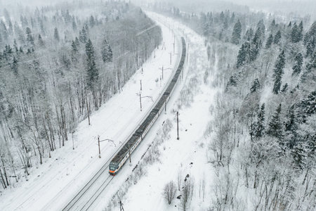 Aerial drone view of train in snow winter forest. Long commuter train moving to railway station